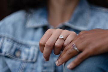 Showing off their engagement rings, a lesbian celebrates their love and their upcoming wedding. They are both wearing jeans, and are Black and multiracial.