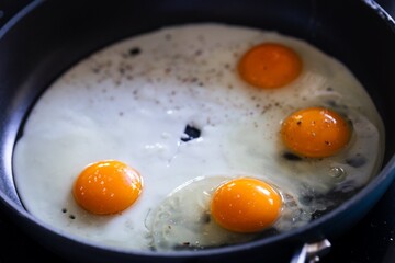 A portrait of a few sunny side up eggs baking in a frying pan. The cook is creating a great breakfast, lunch or brunch. The egg white and the yolk is nicely separated.