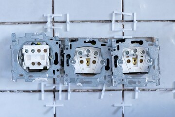 A close up portrait of two electric wall sockets and one light switch without their protective caps...