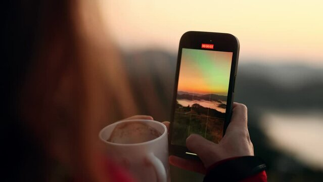 Close up hand of woman hiker taking photos saving great memories on smartphone mobile phone at beautiful sunset in the mountains Pretty girl create content for social media outdoors