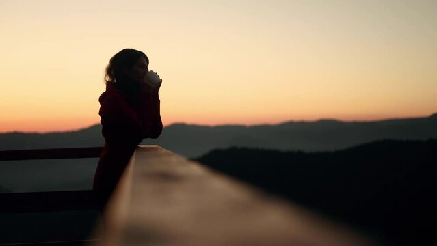 Silhouette of young woman traveler enjoying cup of coffee or tea on warm sunset or sunrise in the mountains Girl taking a sip of coffee or tea with incredible view on the background