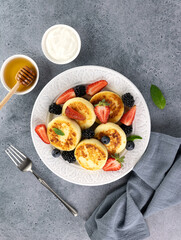 Cottage cheese pancakes, syrniki with sour cream, honey, berries on blue background. Top view. Russian, ukrainian food