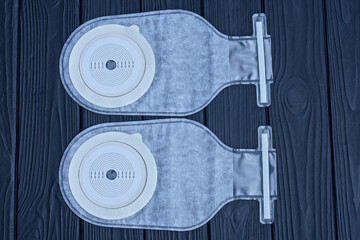  two white medical plastic colostomy bags lie on a black wooden table