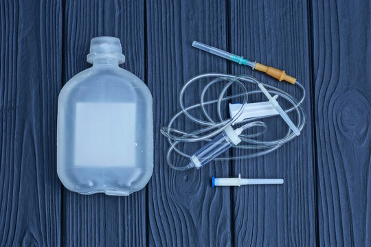 a medical kit of syringes and droplets with a plastic tube and a white bottle of saline lie on a black wooden table