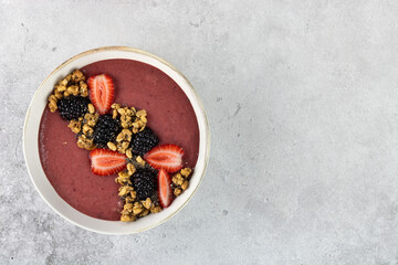 Smoothie bowl with strawberries, blackberries and granola on a gray background. Healthy breakfast. Top view. Copy space.
