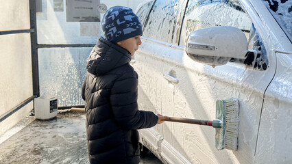 Little boy washing dirty car with soft brish on self service car wash