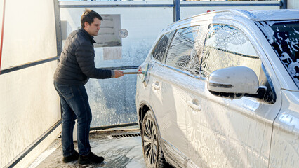 Young man washing his car at self-service carwash. Automobile care, transport cleaning, dirty car.