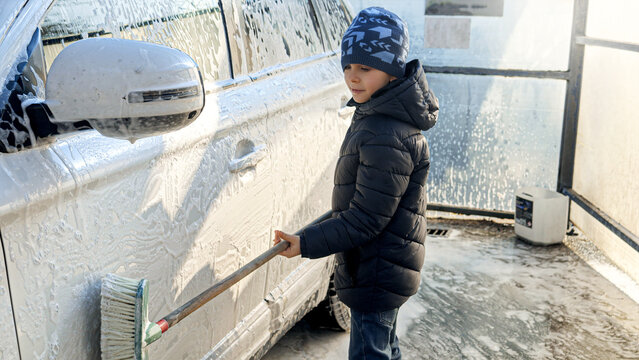 Smiling little boy with brush cleaning and washing car on outdoor car wash