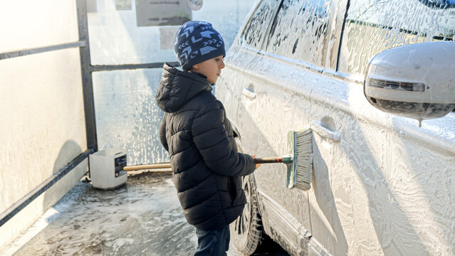 Smiling boy helping washing car with brush and foam. Concept of parenting, children helping parents and automobile care.