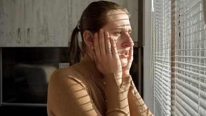 Young scared woman got shocked and terrified after looking outdoors through window blinds.