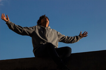 young man sitting on the rooftop with his arms open has a sense of freedom as he gazes at the...