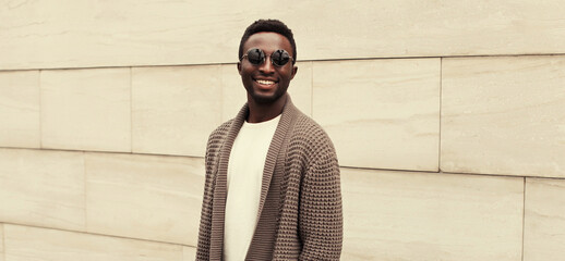 Portrait of stylish smiling young african man wearing brown knitted cardigan on city street...