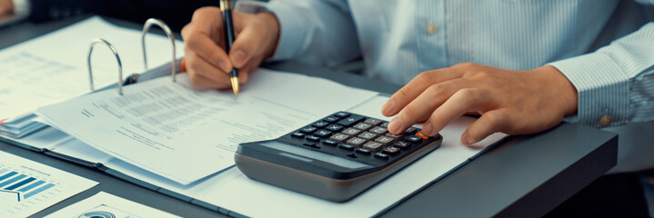 Corporate auditor calculating budget with calculator on his office desk. Dedicated accountant...