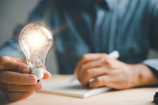 Businessman captures a good idea, holding a light bulb in his left hand. Symbol of solution and success. Working in an inspiring office, the author finds inspiration with a pen on paper.