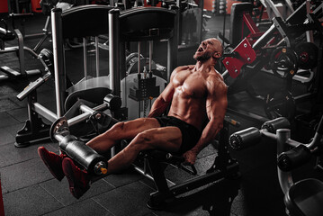 Fototapeta na wymiar Muscular bodybuilder man using weights machine for legs at the gym. Hard training