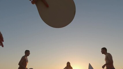 Happy friends playing paddle ball game with rackets on a sandy beach at sunset in the popular island Lefkada, Greece. Slow motion