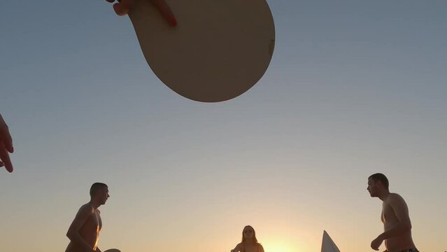 Happy friends playing paddle ball game with rackets on a sandy beach at sunset in the popular island Lefkada, Greece. Slow motion
