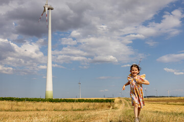 Curious happy girl is running near wind turbine on the field 