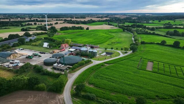 Aerial footage of modern agriculture farm with agricultural fields with corn, biogas plant, wind turbines, photovoltaic panels on the roofs of barns. High-tech farming and renewable resources concept.