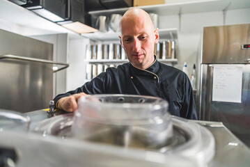 Chef focused on work standing over ice cream maker in kitchen with stainless steel appliances. High...