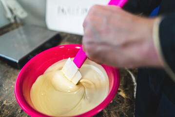 Indoors closeup of hand of chef mixing vanilla ice cream in pink bowl. Handmade ice cream concept. Chef using pink spatua to mix batter. Neutral kitchen background. High quality photo