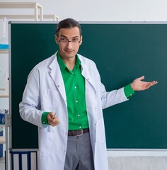 Young male chemist teacher in front of blackboard