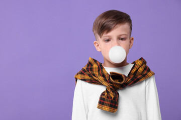 Boy blowing bubble gum on purple background, space for text