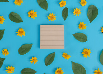 Directly above view of blank notebook with orange flower and green leaf on blue background.