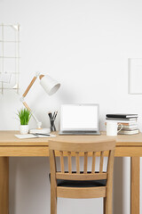 Cozy workspace with laptop, lamp and stationery on wooden desk at home