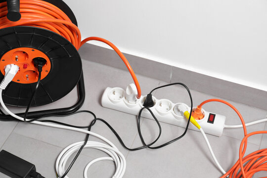 Extension cord reel plugged into power strip on grey floor indoors, space for text