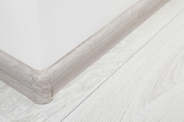 Wooden plinth with connector on laminated floor near white wall indoors, closeup