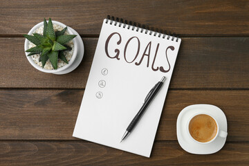 Notebook with empty list of goals, houseplant, pen and cup of coffee on wooden table, flat lay