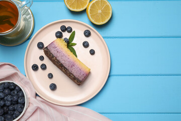 Delicious cheesecake with blueberry, lemon and tea on light blue wooden table, flat lay. Space for text