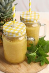 Tasty pineapple smoothie in mason jars, mint and fruit on table, closeup
