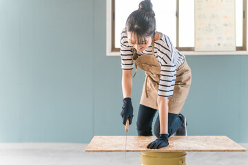 家のガレージでノコギリで木を切るアジア人女性（DIY教室・ワークショップ・日曜大工・体験教室）
 - obrazy, fototapety, plakaty