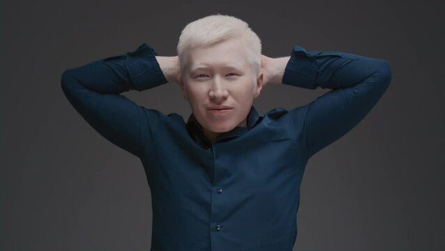 Portrait of an Asian albino guy. Eastern man with a genetic mutation of pigment, white hair. Hands behind his head. The male is wearing a dark shirt in the studio. Abnormal deviations