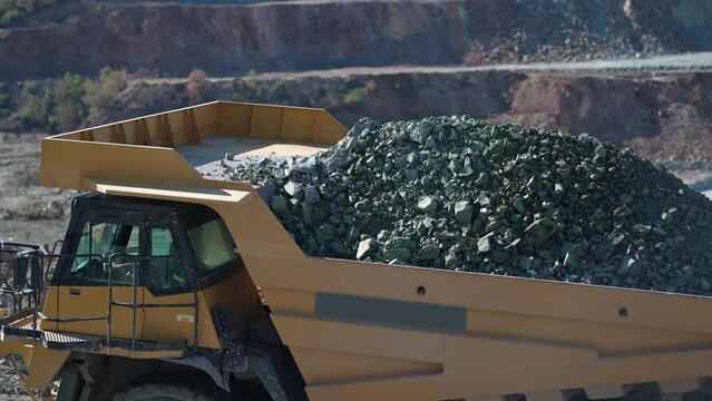 Driving dumper truck transporting ore digged at gold mine pit excavation quarry, slow motion