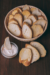 Pieces of roasted white bread in wicker basket and glass bowl of sauce on a dark background. Closeup of delicious croutons.