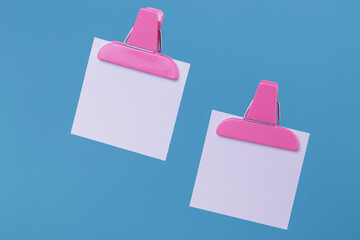 White paper notes with pink paper clip holders isolated on blue background. Blank notes on blue.