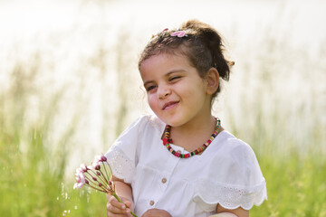 cute little girl child in white dress playing with dandelion by the lake