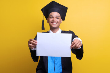 Excited graduate young man in mortar board and bachelor gown holding blank poster with copy space...
