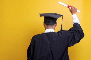 Education and graduation concept. Rear view of a young male graduate with a gown and a cap raising...