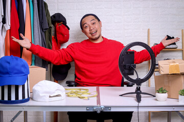 Successful online business owner sitting at his workdesk with arms wide open. Young man with smartphone and shipment box on desk, looking at camera and smiling.