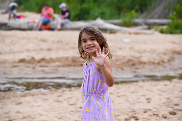 Young brunette girl child on the beach holding up hand showing five fingers. 