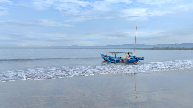 Pangandaran, West Java, Indonesia (April 6, 2023): A wooden boat on the wavy beach on Pangandaran beach.