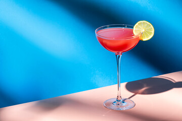 Siesta alcoholic cocktail drink with silver tequila, grapefruit and lime juice, syrup and italian red bitter liqueur, summer blue bright background, hard light and shadows