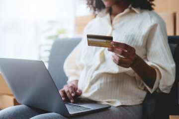 Woman using laptop computer and credit card for online shopping at home. Female happily utilizes her laptop and credit card for convenient online purchases.