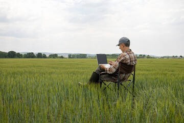 man farmer working with laptop on wheat field. Smart farming.