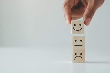 Customer satisfaction concept. Hand lifts smiling face and sad face icon on wood cube block. customer services best excellent business rating experience. Satisfaction survey concept.