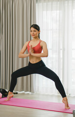 Exploring digital asanas, a beautiful Asian woman practices yoga at home with her tablet, deepening her connection to body and soul.